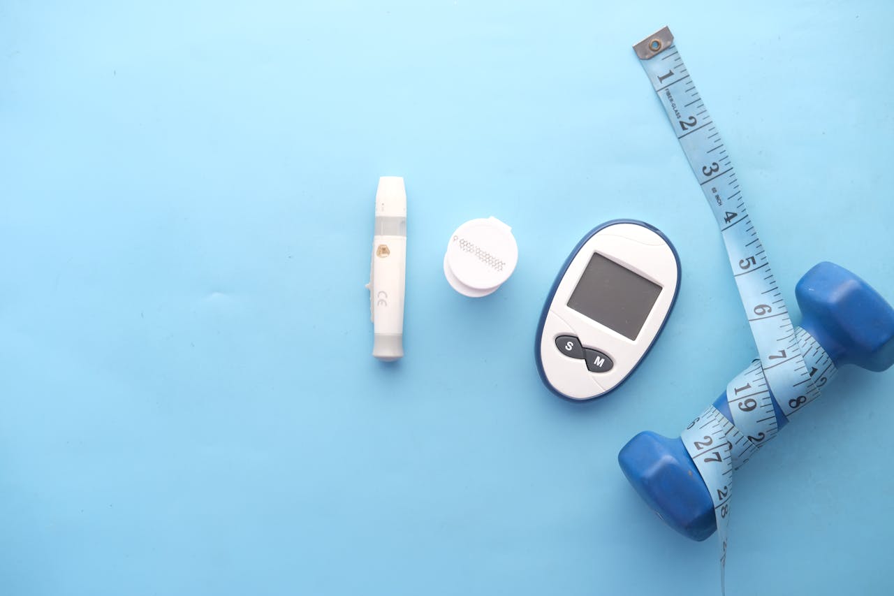 Top view of fitness and health equipment including dumbbell, glucometer, and measuring tape on a blue background.